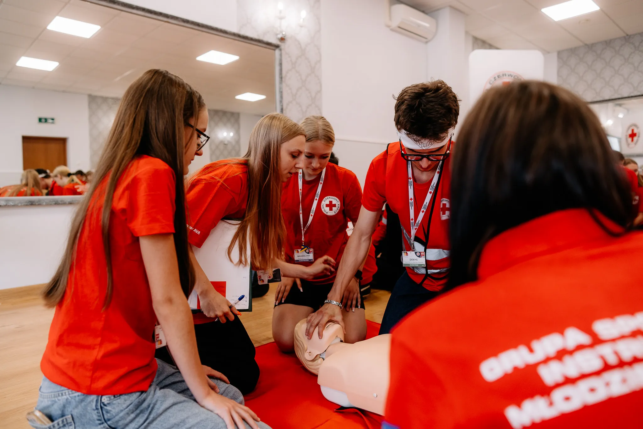 Młoddzi ludzie siedzą przy fantomie podczas kursu pierwszej pomocy